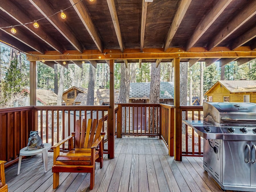 A covered deck with wooden railings, a grill, and seating.