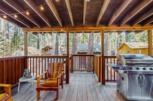 A covered deck with wooden railings, a grill, and seating.
