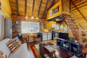 A cozy cabin with a wooden interior, a dining area, a kitchen, and a staircase.