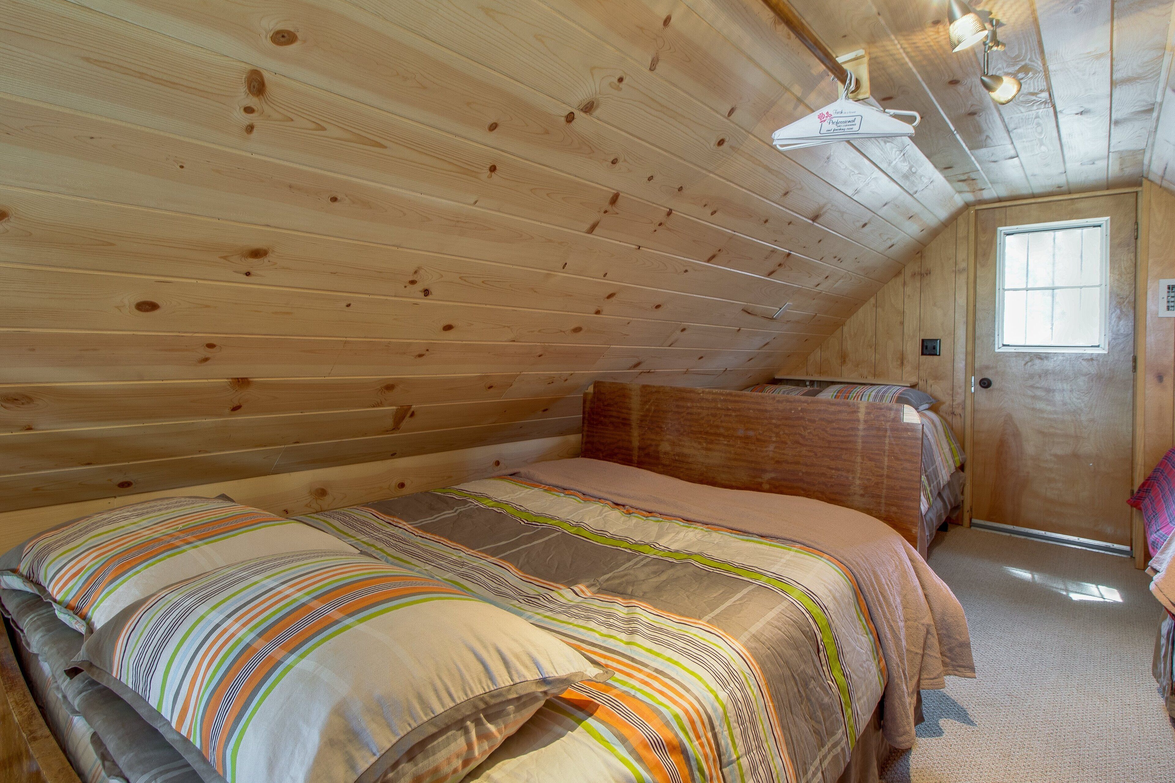 Un dormitorio acogedor en el ático con paredes de madera y techo inclinado.