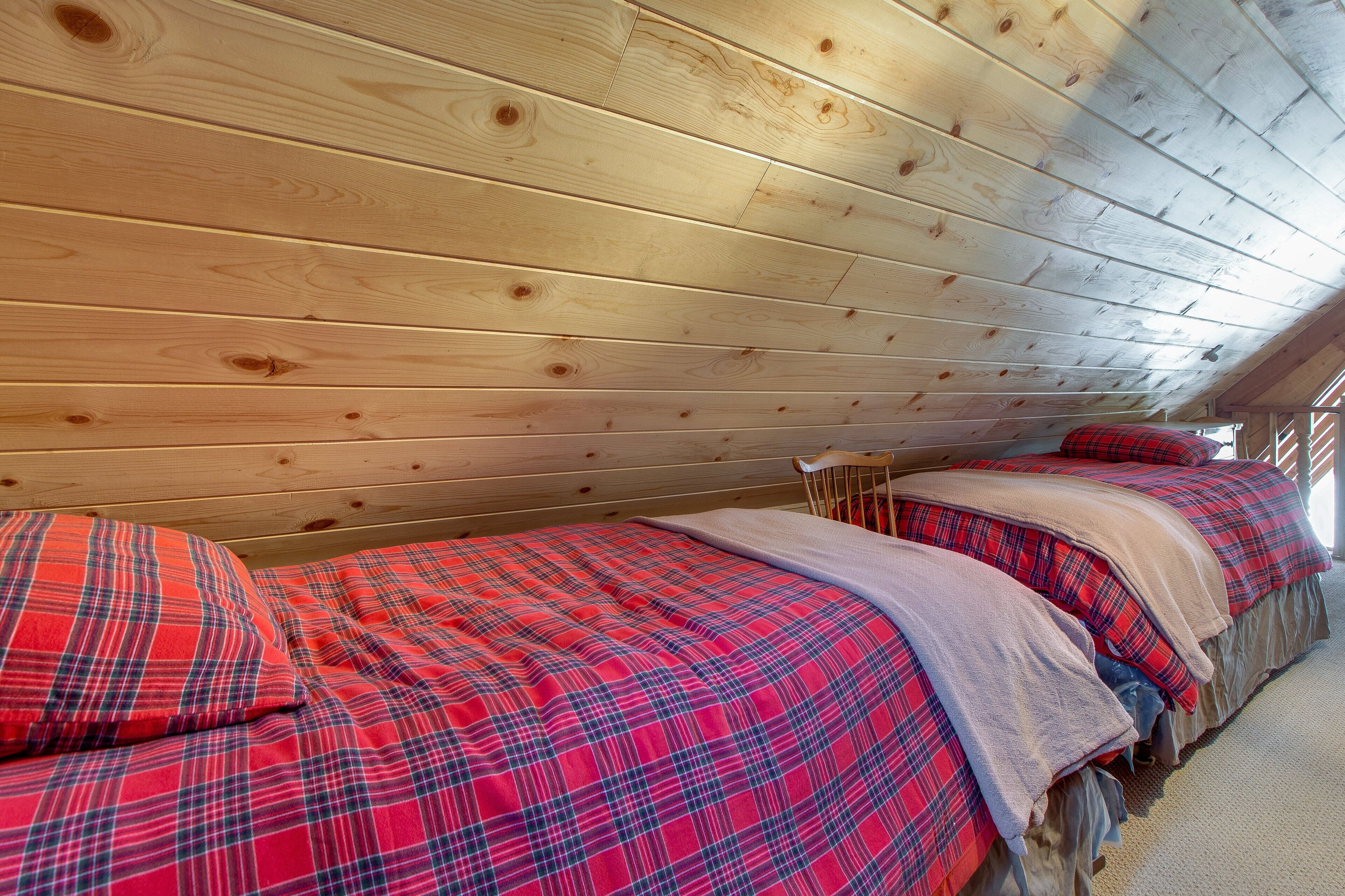 Une cabane aux murs en bois et au plafond incliné. On y trouve trois lits avec une literie à carreaux rouges et bleus.