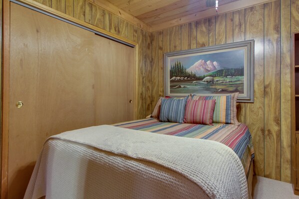 A wooden-paneled room with a bed, a painting of a landscape, and a door.