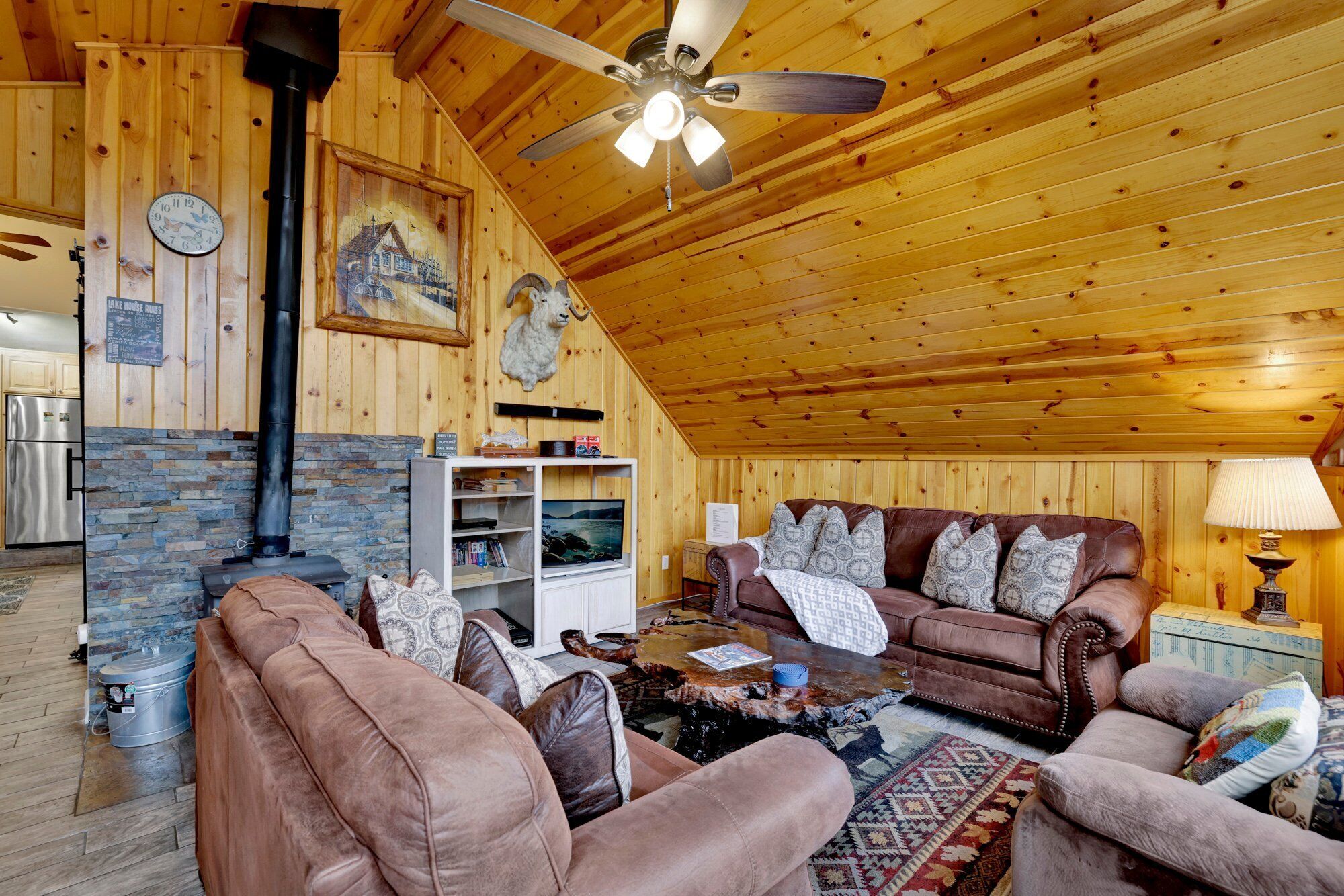 Een gezellig houten cabin interieur met een open haard, een plafondventilator en een stenen muur.