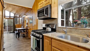 Une cuisine dotée de meubles en bois, d’un évier en acier inoxydable, d’une cuisinière et d’une fenêtre donnant sur une forêt.