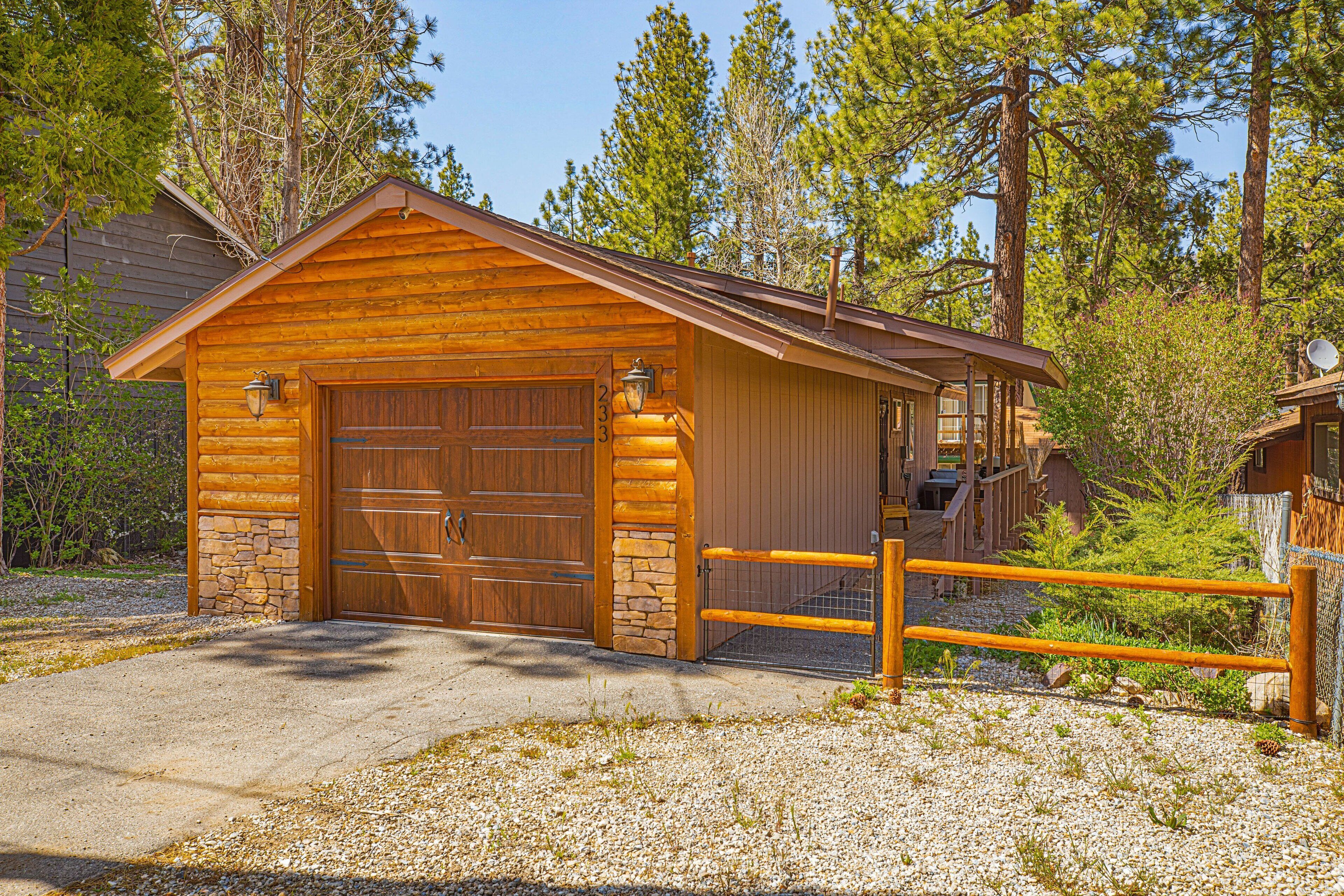 A log cabin with a stone foundation, a large wooden garage door, and a gravel driveway.
