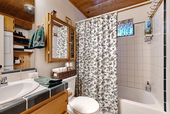 Une salle de bain avec un meuble-lavabo en bois, une baignoire et un rideau de douche à motifs floraux.