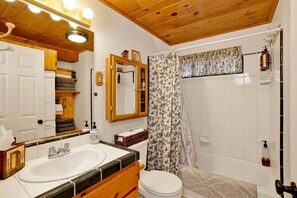 Une salle de bain avec un plafond en bois, un lavabo blanc, des toilettes et un rideau de douche.