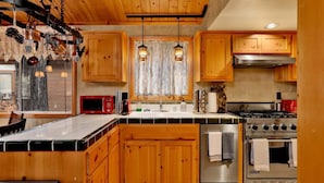 A kitchen with wooden cabinets, a stove, a microwave, and hanging pendant lights. - Craftsman Hideaway #630 (Big Bear Lake)