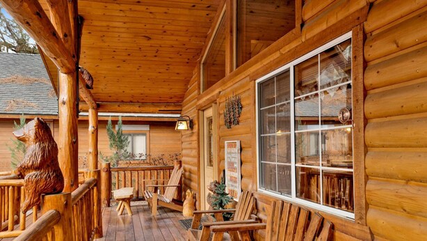 A wooden cabin with a porch, wooden chairs, a bear sculpture, and a sign with text. - Craftsman Hideaway #630 (Big Bear Lake)