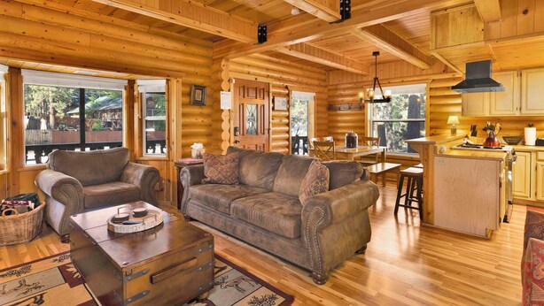 Ein Holzblockhaus-Interieur mit einem Holzespeise-Tisch, einem Ledersofa und einer Küchenzeile mit Holzschränken und einem Herd.