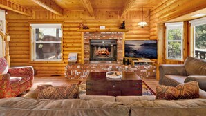 Ein rustikales Blockhaus-Interieur mit Kamin, Holzwänden, einer Couch und einem Fernseher.