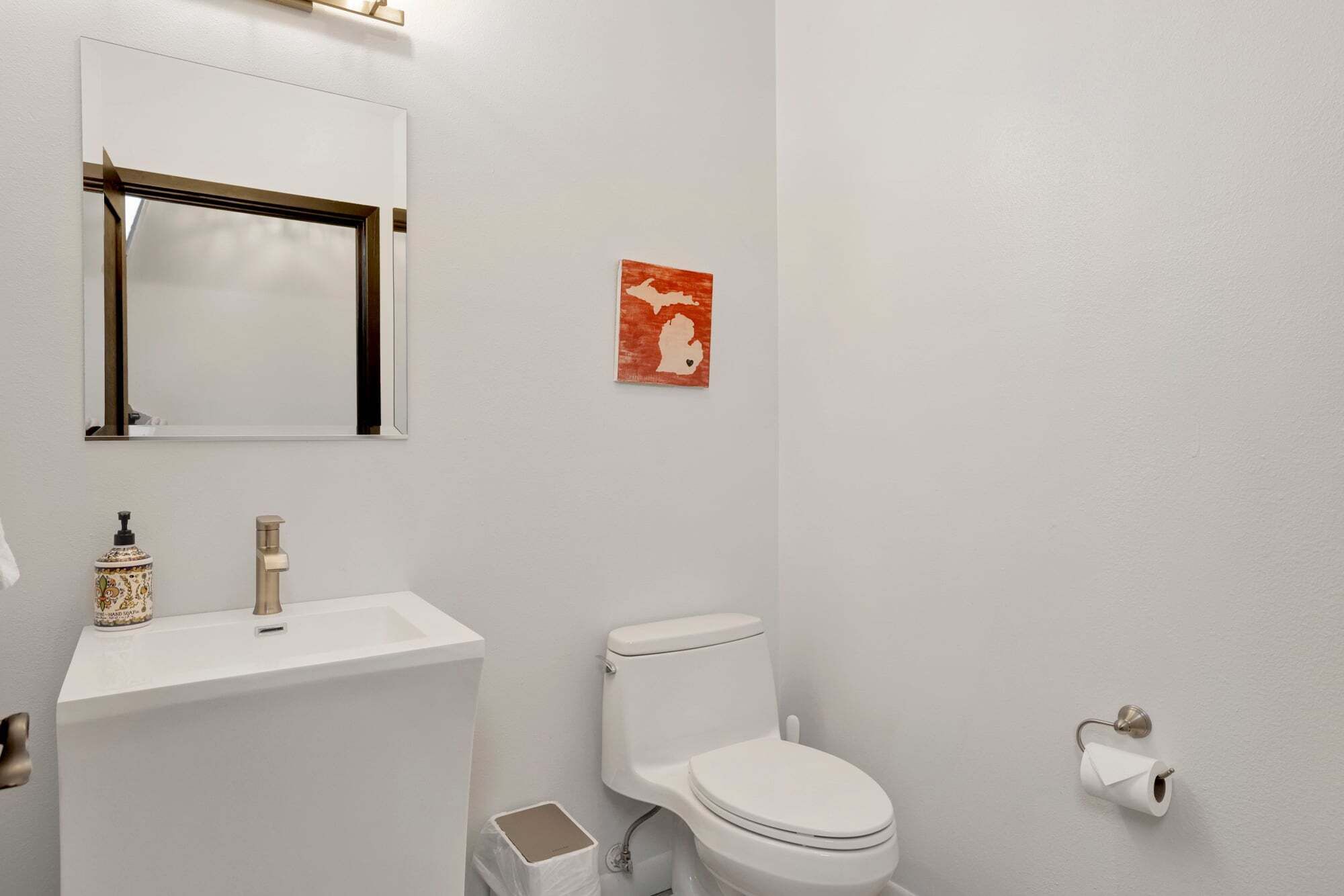 A bathroom with a white sink, a toilet, a mirror, and a red artwork on the wall.