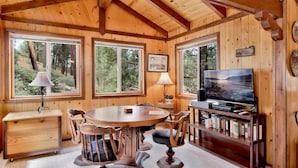 A cabin interior with a wooden interior, a round dining table, chairs, a television, and a bookshelf. - Idle Ours Cabin #713 (Fawnskin)