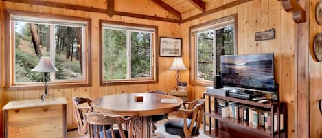 A cabin interior with a wooden interior, a round dining table, chairs, a television, and a bookshelf.