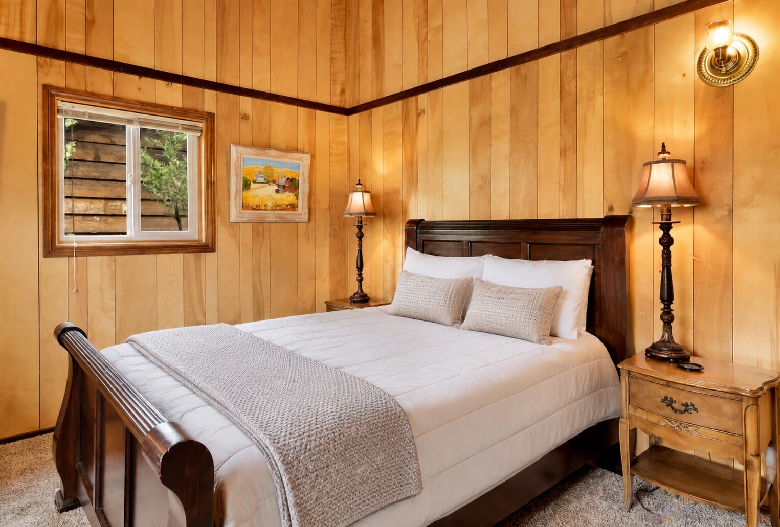 A wooden-paneled bedroom with a bed, two bedside lamps, a nightstand, and a window with blinds.
