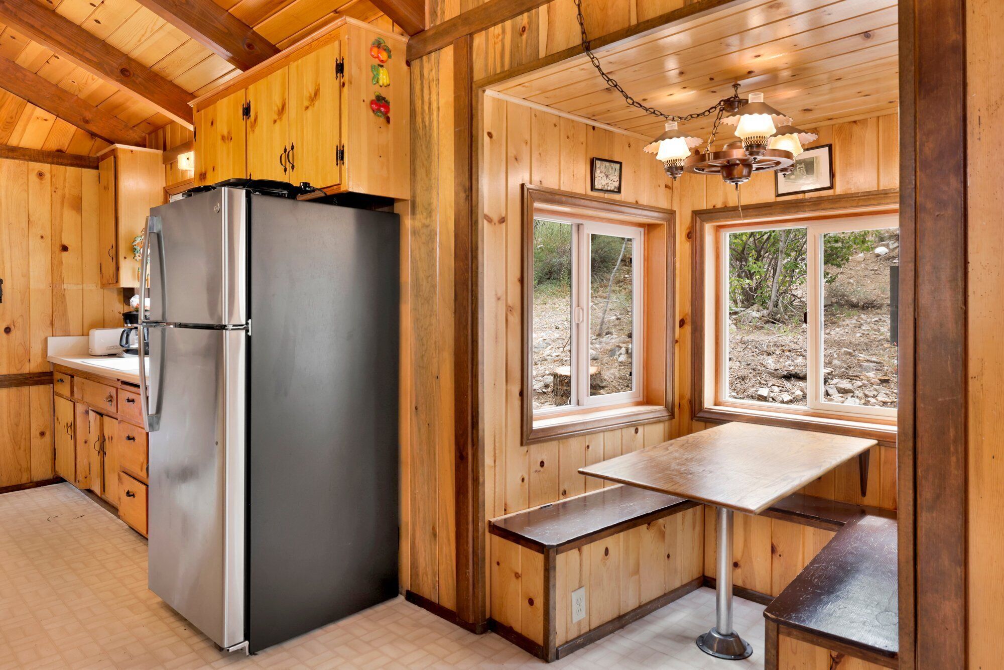 Una cucina in baita di legno, con frigorifero, mobili impiallacciati, una finestra e un tavolo.