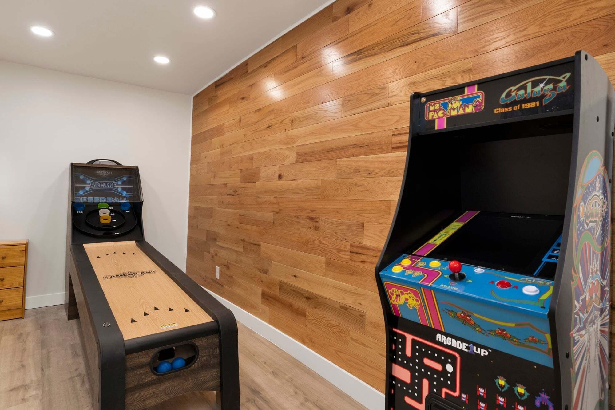 A room with wooden flooring, a ping pong table, and two arcade machines.