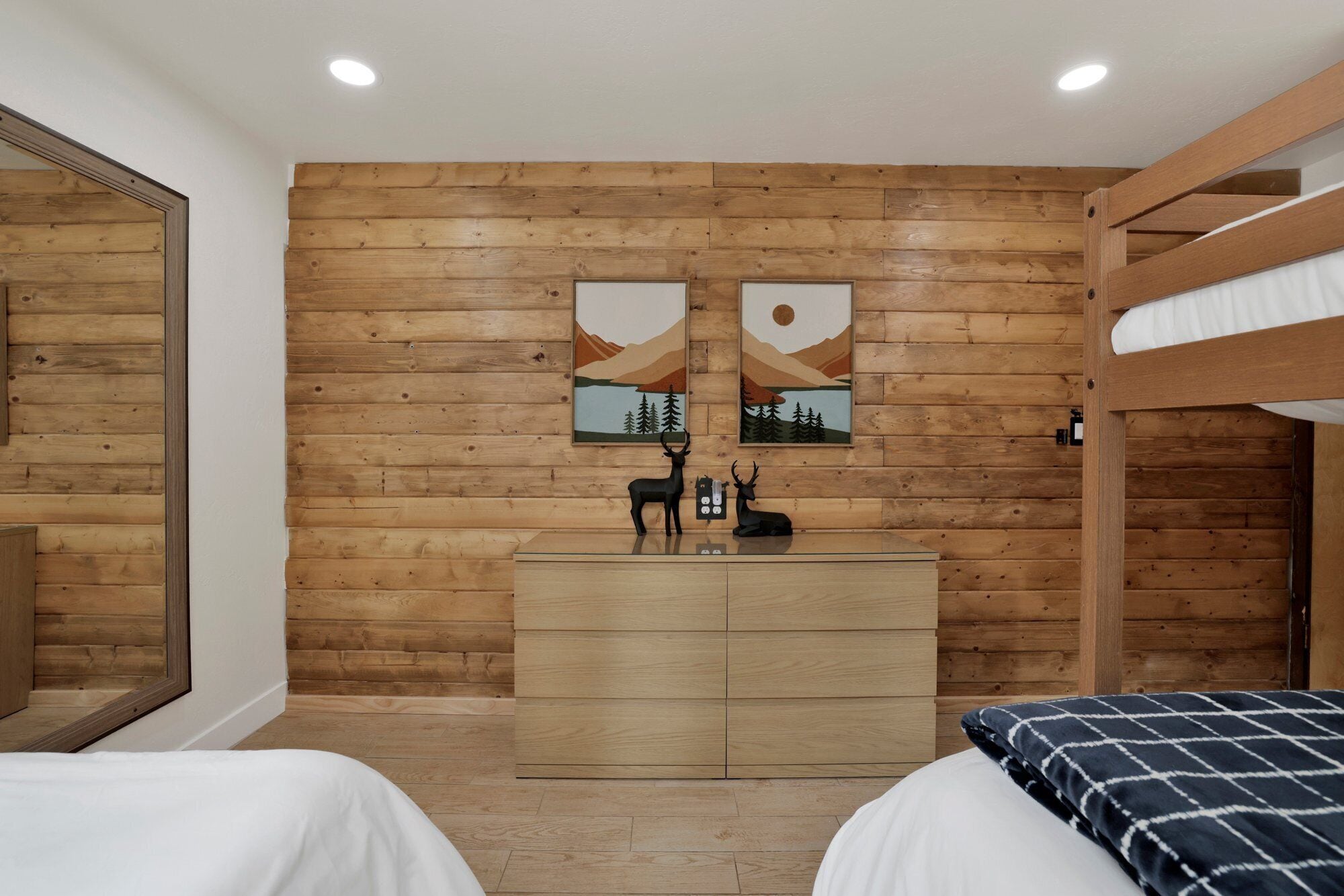 Une pièce aux murs recouverts de lambris en bois, avec une commode en bois, deux lits et deux tableaux accrochés au mur.