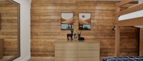 Une pièce aux murs recouverts de lambris en bois, avec une commode en bois, deux lits et deux tableaux accrochés au mur.