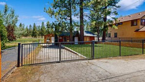 Une propriété clôturée comprenant une petite cabane et un bâtiment plus grand, le tout entouré d’arbres.