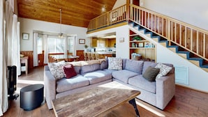 Un vaste espace de vie comprenant un grand canapé d’angle, une table basse en bois et un escalier avec des rampes en bois menant à un niveau supérieur.
