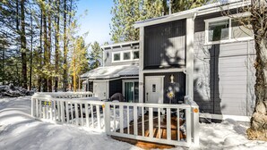 A two-story cabin with a white deck and a covered porch, surrounded by a snowy landscape and tall trees. - Moose-in' Around (Big Bear Lake)
