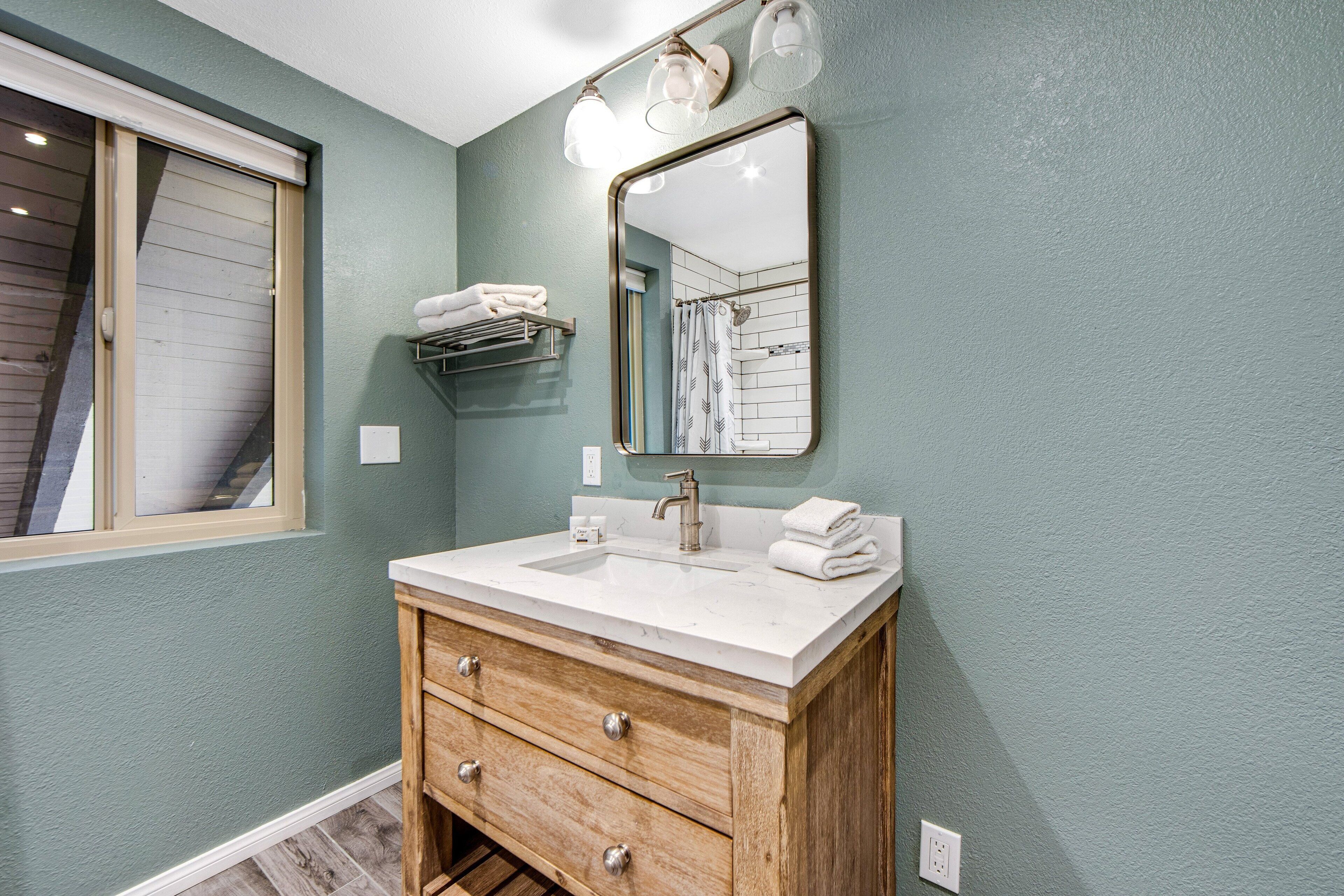 Une salle de bain avec un meuble-lavabo en bois, un lavabo blanc, un miroir avec éclairage intégré et un porte-serviettes.