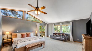 A bedroom with a large bed, a bench, a ceiling fan, a TV, and a window with curtains. - Mt Doble Dream Home #504 (Big Bear City)