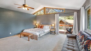 A bedroom with a bed, bedside tables, a bench, a ceiling fan, and a view of the outdoors. - Mt Doble Dream Home #504 (Big Bear City)