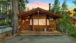 A wooden cabin with a porch, a mailbox, and a sign indicating a 4-room cabin with a 1-car garage. - Orchard Family Cabin #2560 (Big Bear Lake)