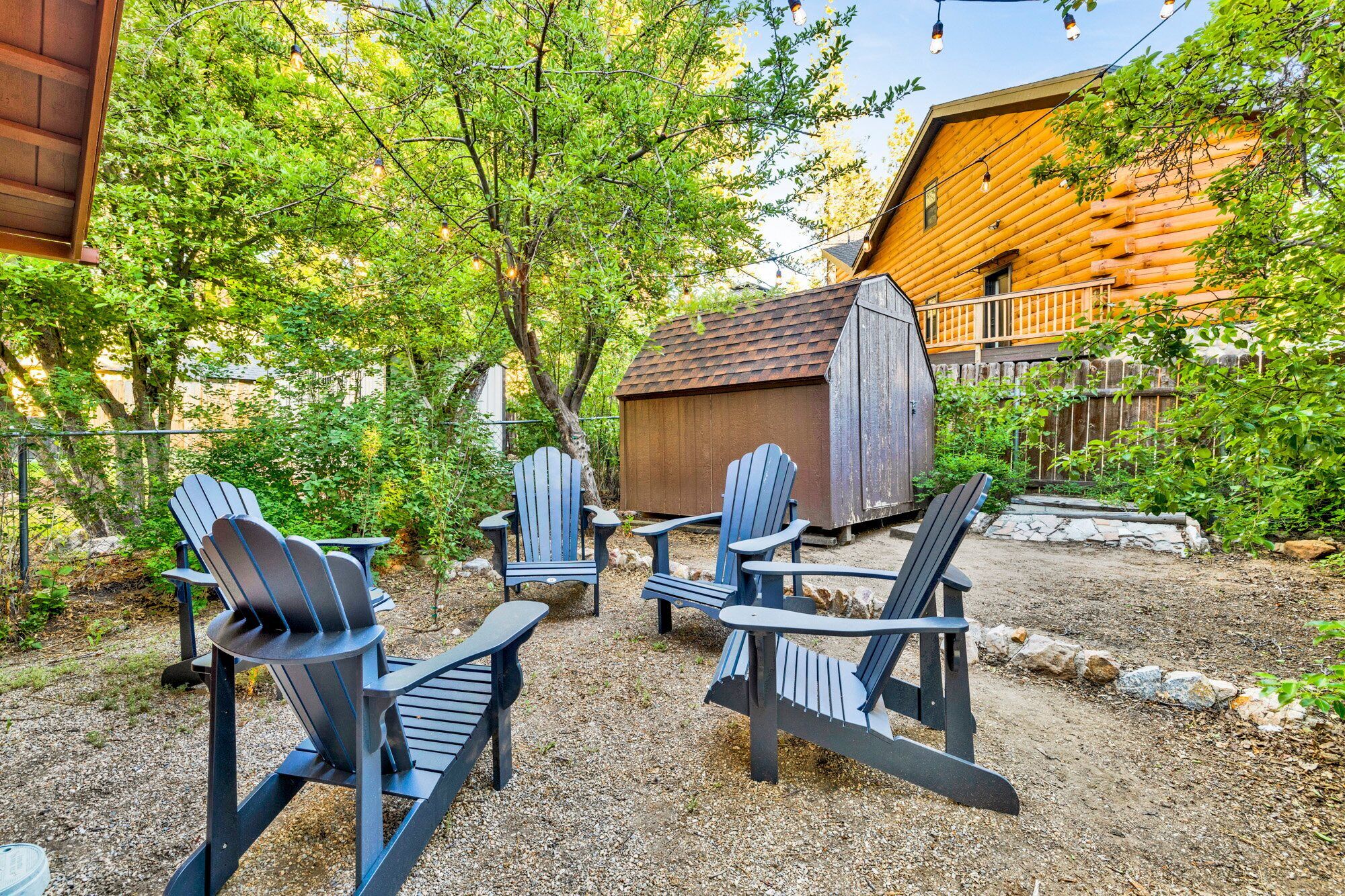 A rustic outdoor seating area with Adirondack chairs, a wooden shed, and a wooden building with a sloped roof.