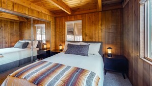 Een slaapkamer in een houten chalet met twee bedden, een grote spiegel en een raam.