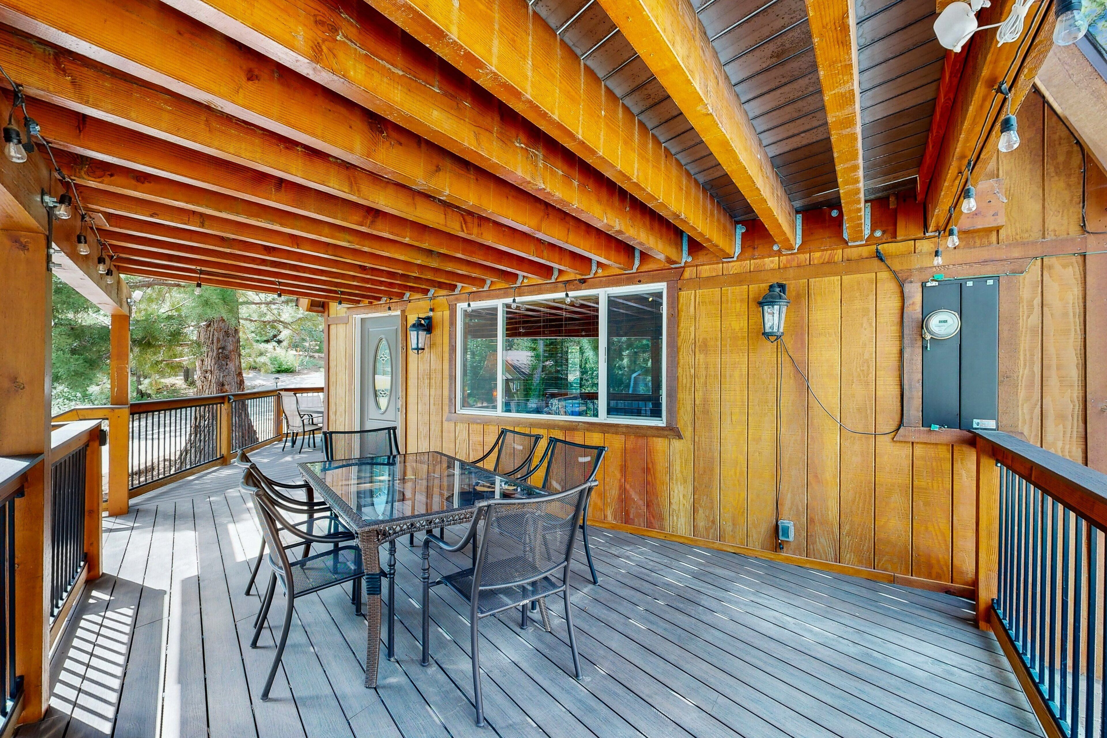 A wooden deck with a glass table and chairs, surrounded by wooden railings and a view of trees.