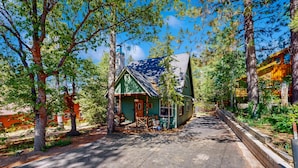 Une cabane rustique avec un toit végétalisé, entourée de grands arbres et sous un ciel dégagé.
