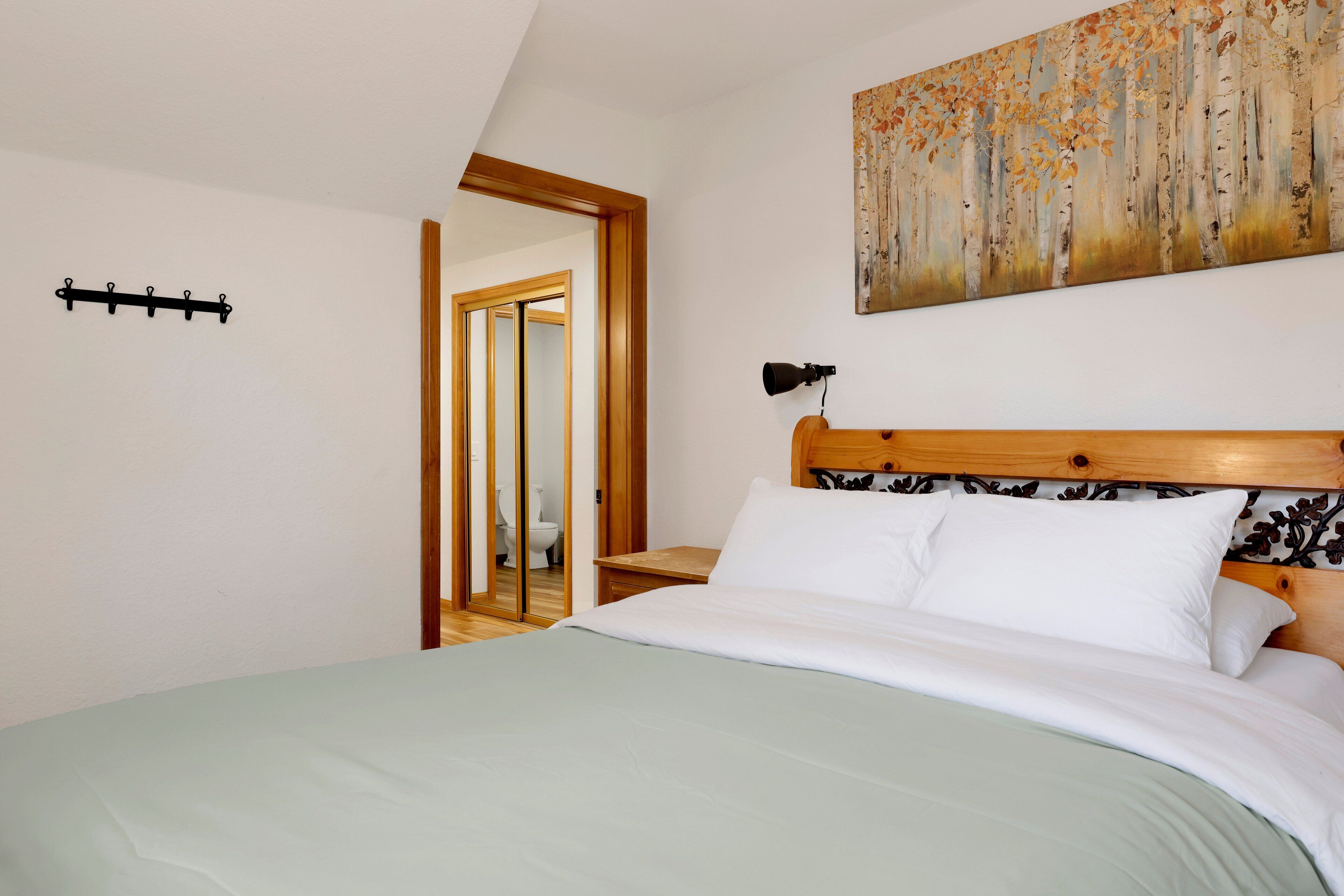 A bedroom with a bed, a wooden headboard, a painting on the wall, and a door leading to another room.