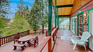 A wooden deck with a table and chairs, surrounded by a railing, overlooking a forested area. - Rooster's Den #710 (Big Bear Lake)