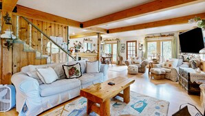 A spacious living room with a light blue sofa, wooden beams, a staircase, and a television. - Rooster's Den #710 (Big Bear Lake)