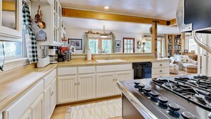 A spacious kitchen with white cabinetry, a large stove, and a window with curtains. - Rooster's Den #710 (Big Bear Lake)