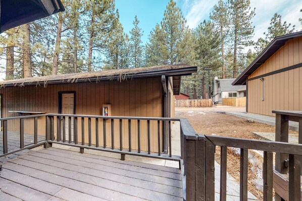 A wooden deck with a metal railing, a small building with a door, and a forested background.