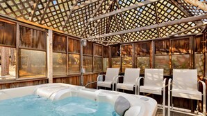 Un espace détente avec un bain à remous, doté de murs en bois et d’un plafond ajouré, comprenant quatre chaises blanches et un grand bain à remous.