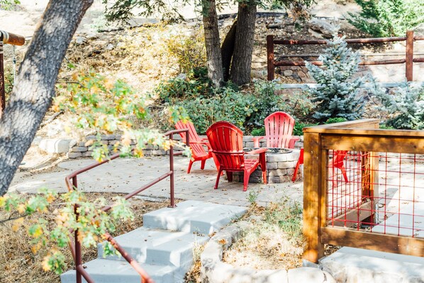 A patio area with red chairs and a table, surrounded by stone steps and a wooden fence. - The Refugio #2552 (Big Bear Lake)