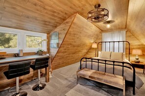 Un dormitorio con cama, escritorio, silla, banco y una lámpara colgante.