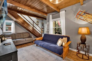 Habitación estilo loft con techo de madera, un sofá azul, una mesa de centro de madera y una lámpara.