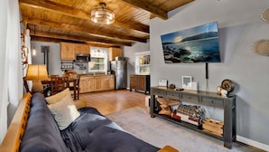 A modern living room with a sofa, a dining area, a kitchen with wooden cabinets, a mounted TV, and a fireplace. - The Summit at Sherwood #618 (Big Bear City)