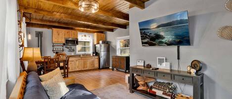 A modern living room with a sofa, a dining area, a kitchen with wooden cabinets, a mounted TV, and a fireplace.