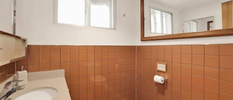 Un baño con un lavabo blanco, paredes de azulejos marrones, suelo de madera, una ventana y un espejo.