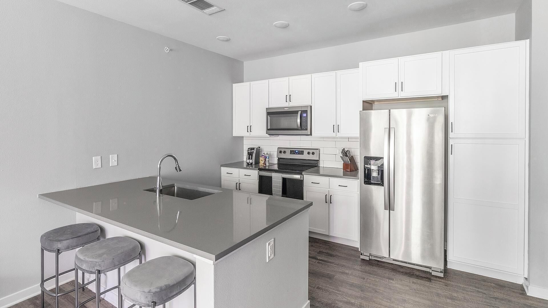 A modern kitchen with white cabinets, stainless steel appliances, a central island with stools, and a built-in oven.
