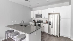 A modern kitchen with white cabinets, stainless steel appliances, a central island with stools, and a built-in oven.