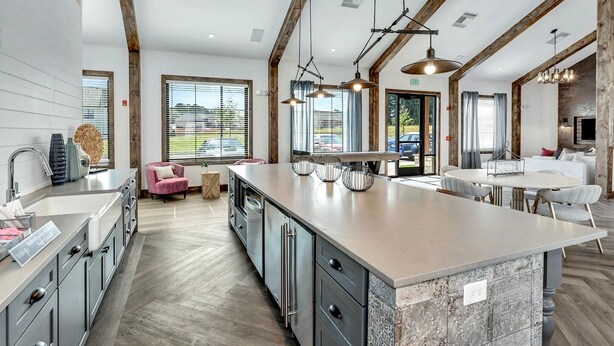 A modern kitchen with a large island, wooden beams, and large windows.