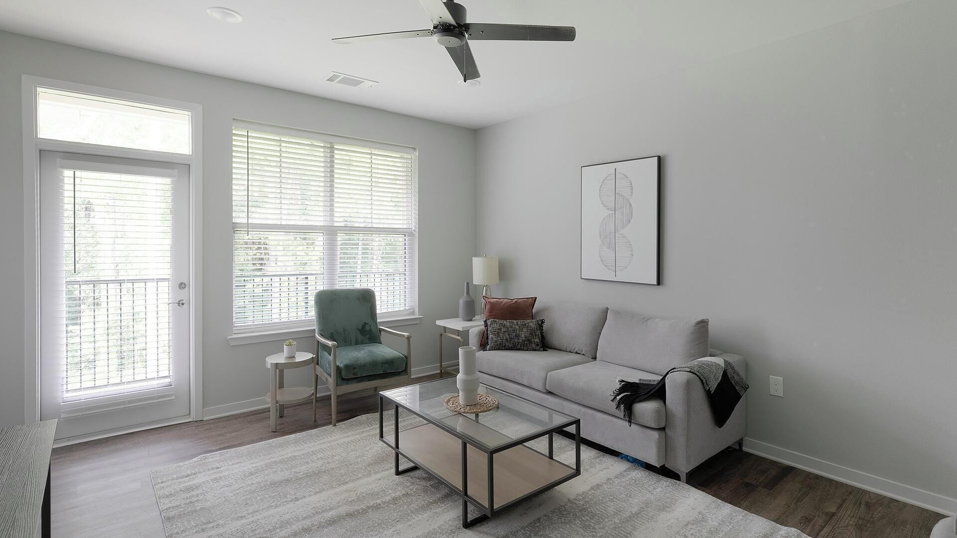 A living room with a grey sofa, a green armchair, a coffee table, and a ceiling fan.